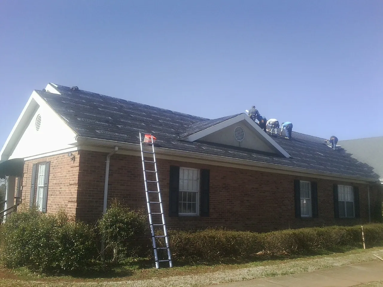 Crew tearing shingles off a brick ranch roof with a ladder set — Emergency Roof Repair work by our crew in Atmore