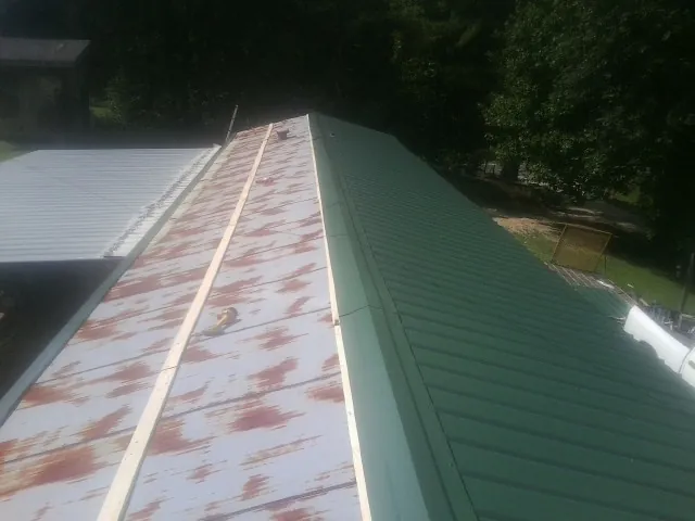 Old rusted panels beside newly installed green metal roofing — Wind Damage Roof Repair by Roofing Brothers in Atmore