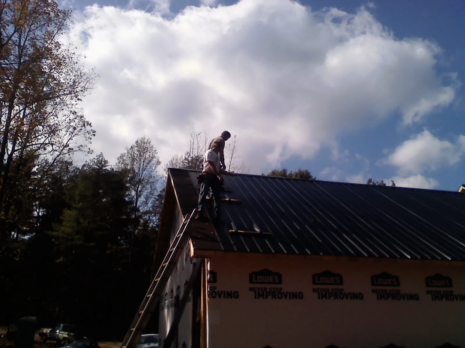 Roofer fastening dark metal panels high against a cloudy sky, from a Roof Inspection job in Atmore