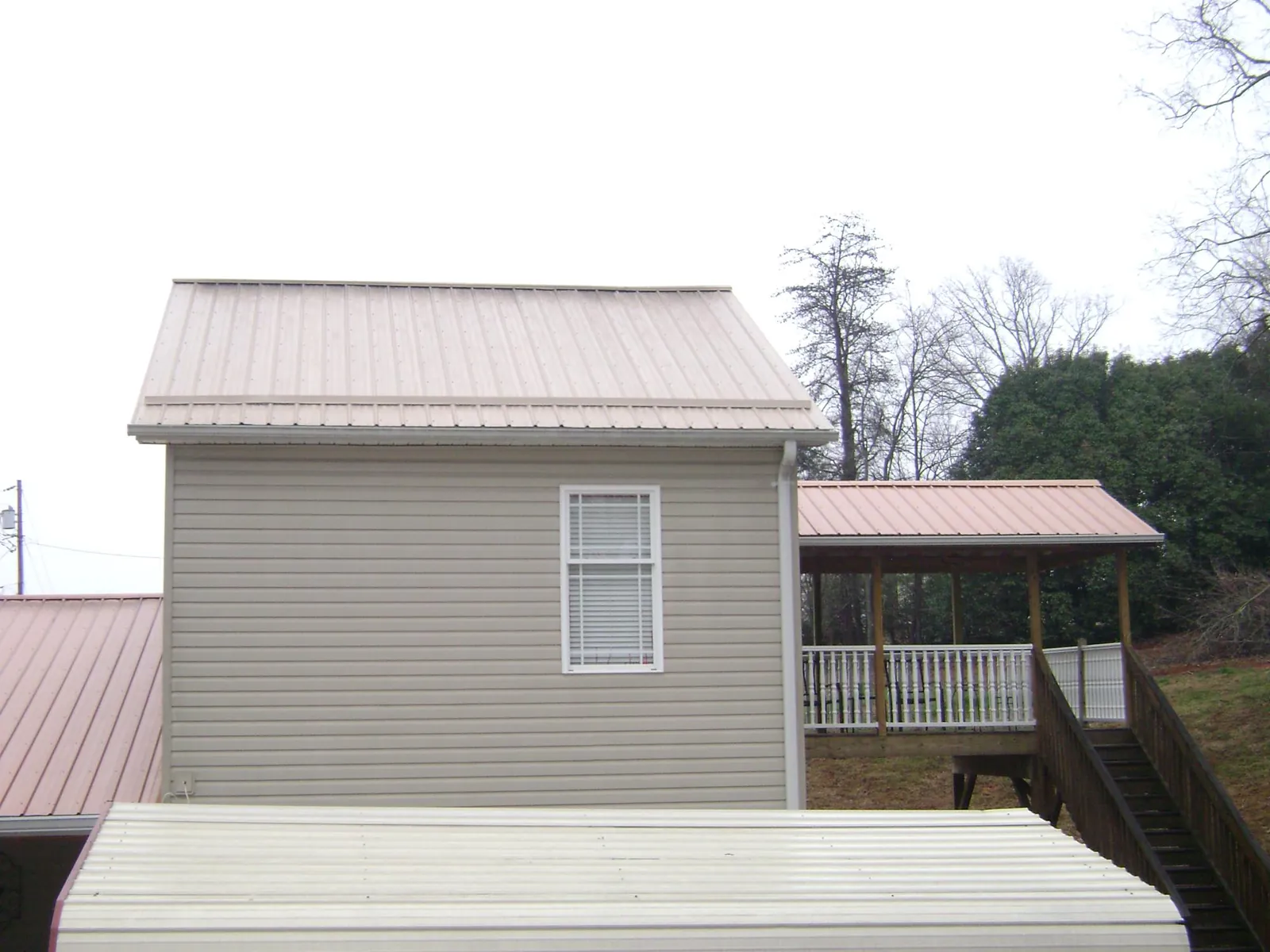 Tan metal roofs on a two story addition and attached porch, from a Roof Replacement job in Atmore